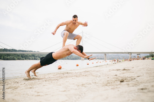 Two young attractive men having fun on beach and doing some fitness workout. 