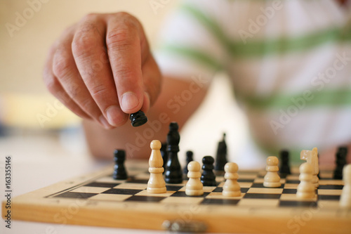 Senior man playing chess, close-up of hand.