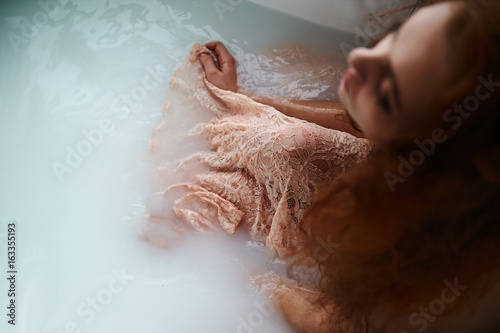 Beautiful romantic red-haired girl sitting in the bath .The face is not visible. In lace dress powdery pastel cream color