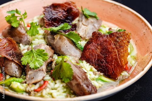 Baked duck served in a plate with rice and green beans and greens dressed with sauce.