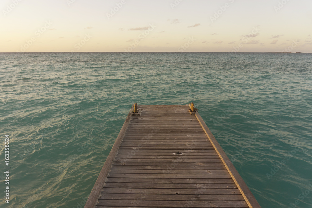 Wooden pier over tropical sea at sunset