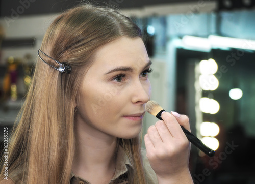 Make-up artist makes make-up at the face  and looking at the mirror