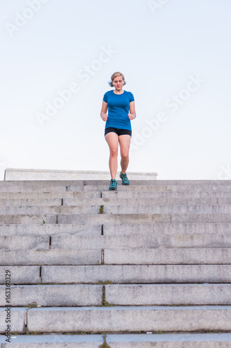 Fototapeta Naklejka Na Ścianę i Meble -  Young fit woman running down steps outside during workout