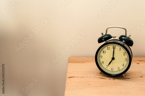 black vintage retro alarm clock times at 7 o'clock morning on wooden table, selective focus, copy space, vintage color tone