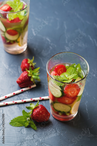 Cold and refreshing infused detox water with strawberry and cucumber in glass on black background.