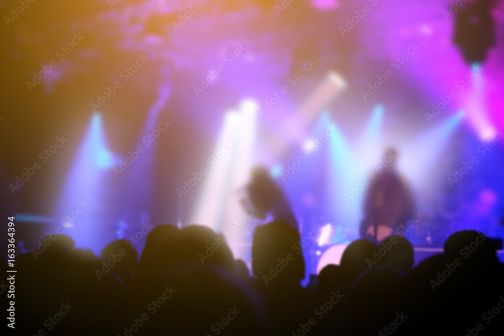 Blurred background, Bokeh, silhouette of cheering audience, hands up and musicians on the stage with lighting in indoor concert