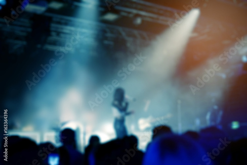 Blurred background, Bokeh, silhouette of cheering audience, hands up and musicians on the stage with lighting in indoor concert