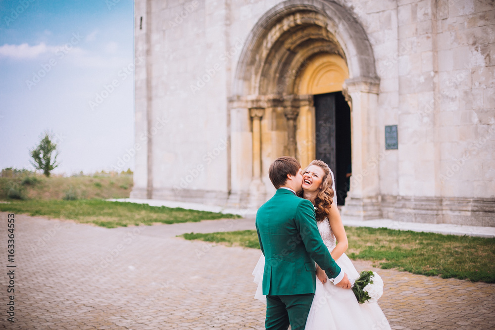 gorgeous wedding couple . The happinest brides embracing near castle. Groom and bride embrace on a background of the castle. very lucky in love wedding day. The groom holds the bride on hands