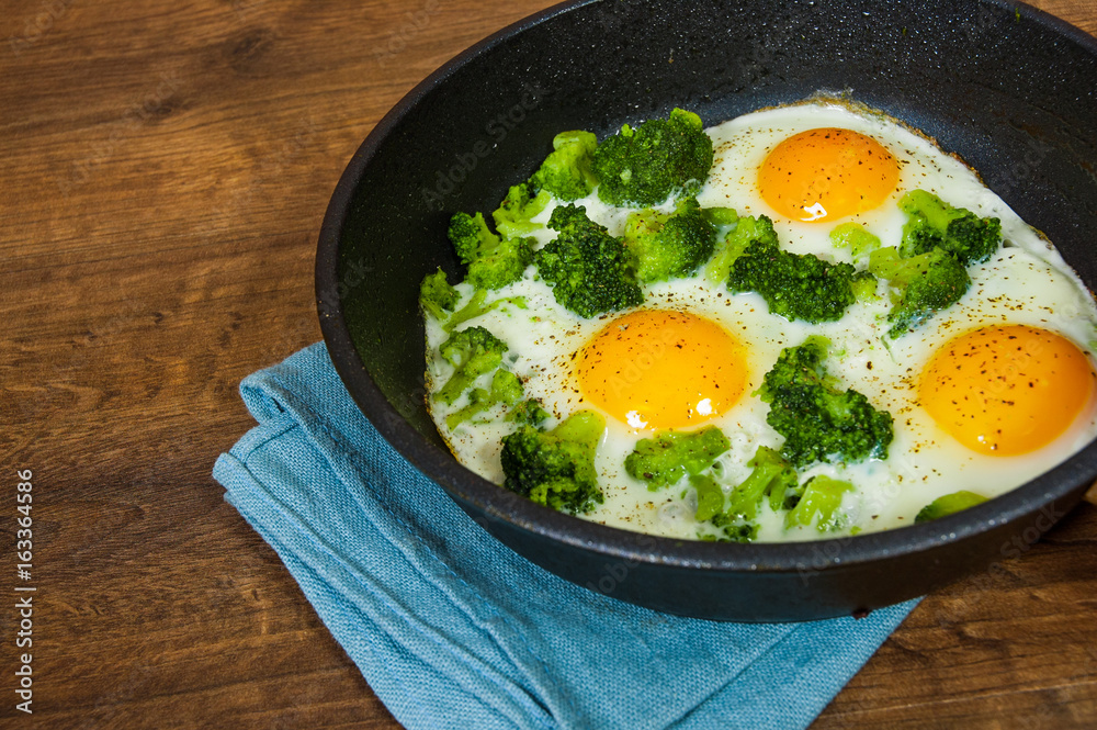 Fried eggs with broccoli in a iron frying pan on the brown wooden table background. with copy space.