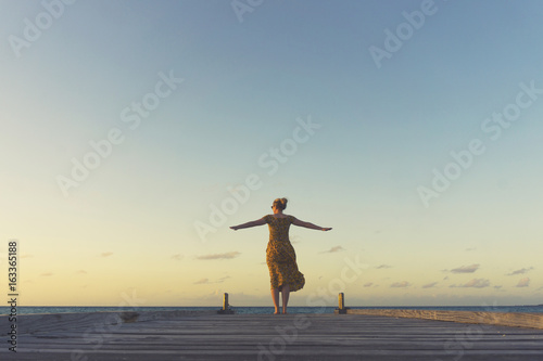 Female traveller at the end of a wooden pier at sunset