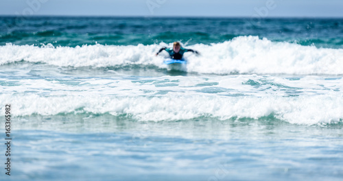 Photography Surfer woman with surfboard is paddling on the wave.