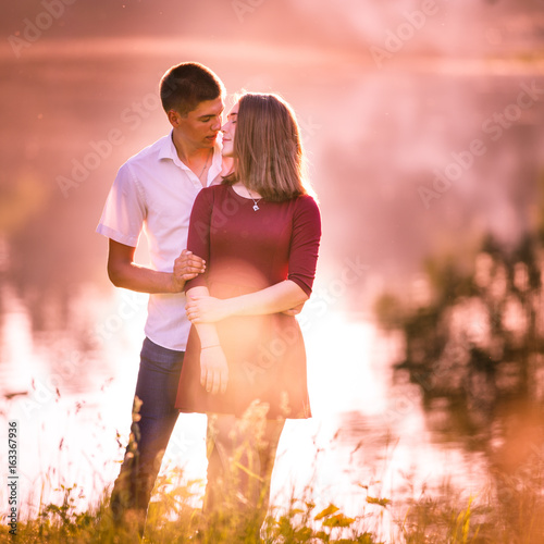 Portrait of a beautiful young couple in love standing and kissing near the river.