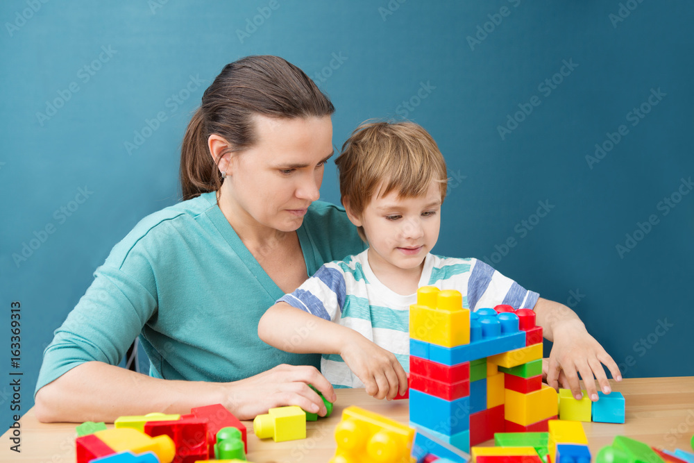 mother and little son  playing with lots of colorful plastic blocks constructor indoor.  The happy family spends time together at home.