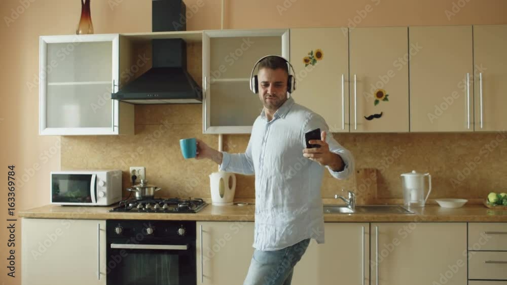 Handsome young funny man in headphones dancing and singing in kitchen at home in the morning and have fun on vacation Handsome young funny man in headphones dancing and singing in kitchen at home in the morning and have fun on vacation