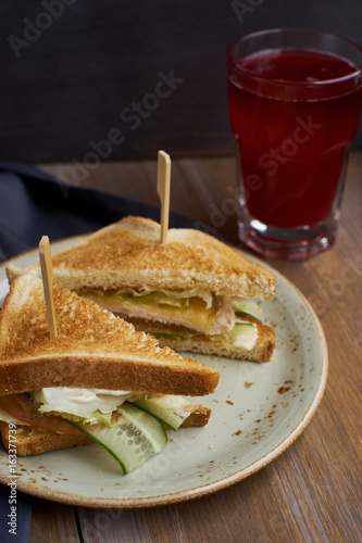 Club sandwich with cheese, ham, lettuce and cucumber on plate and glass of cranberry juice