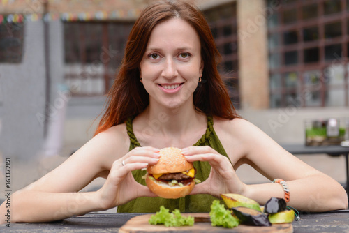 Smiling woman eating cheeseburger outdoors