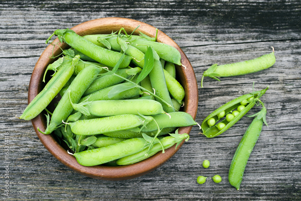 Pods of green peas in a round plate on an old wooden surface, top view Pods of green peas in a round plate on an old wooden surface, top view