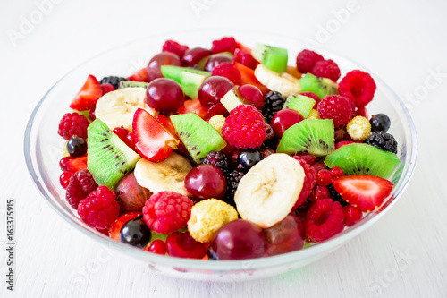 Fresh fruit salad in bowl on white rustic table.