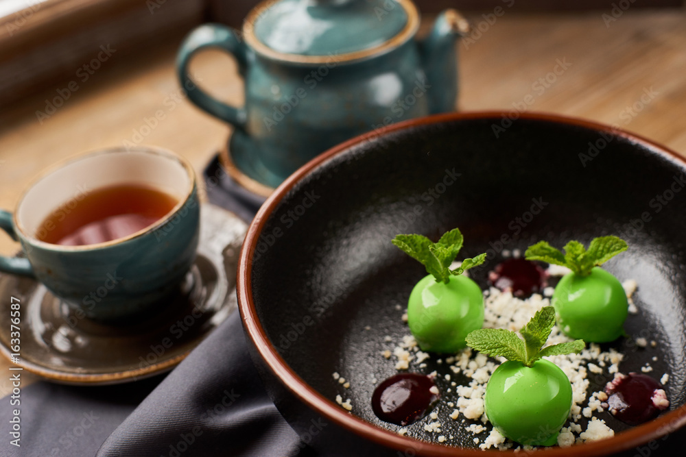 Small green apples desert with chocolate, mint leafs and caramel served in big black plate. Hot black tea. Small green apples desert with chocolate, mint leafs and caramel served in big black plate. Hot black tea.