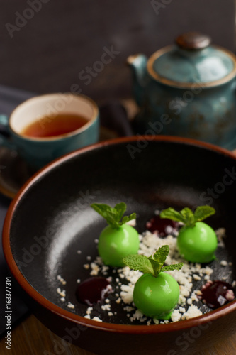 Chef's dessert from apples, chocolate, mint and caramel glazed in form of small apples with leafs. Served with teapot and cup of hot black tea.