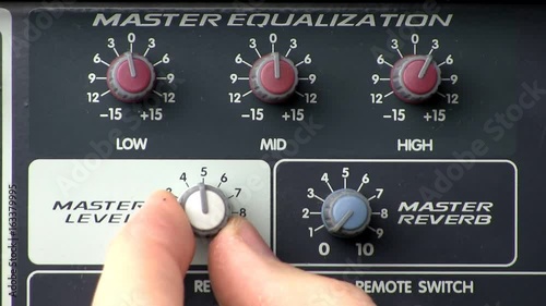 A man makes adjustments to master level, reverb and equalizer control knobs on powered audio mixer