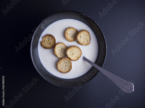 Danish koldskaal - cold buttermilk soup with crispy biscuits named kammerjunker served in rustic black bowl, isolated on black background
