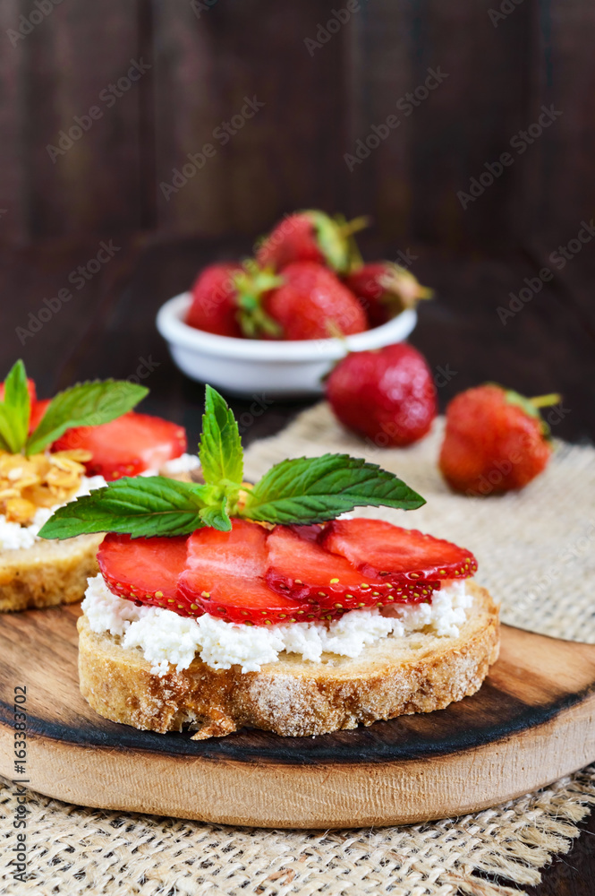 A small bruschetta with curd and fresh strawberries on a dark wooden background. Proper nutrition. Vertical view.