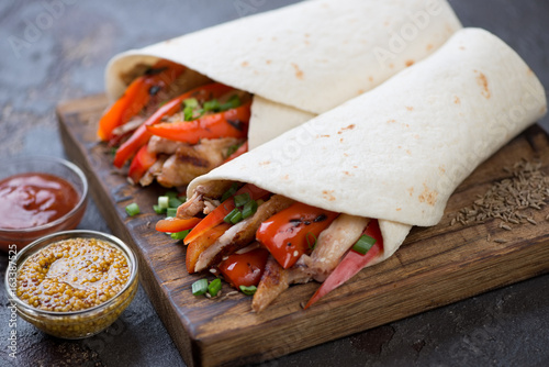 Tortilla wraps filled with grilled chicken meat and vegetables served on a wooden chopping board
