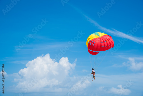 People enjoy parasailing water sport, Flying on a parachute behind a boat on a summer holiday by the sea at Patong beach. The most famous tourist attraction in Phuket province, Thailand.