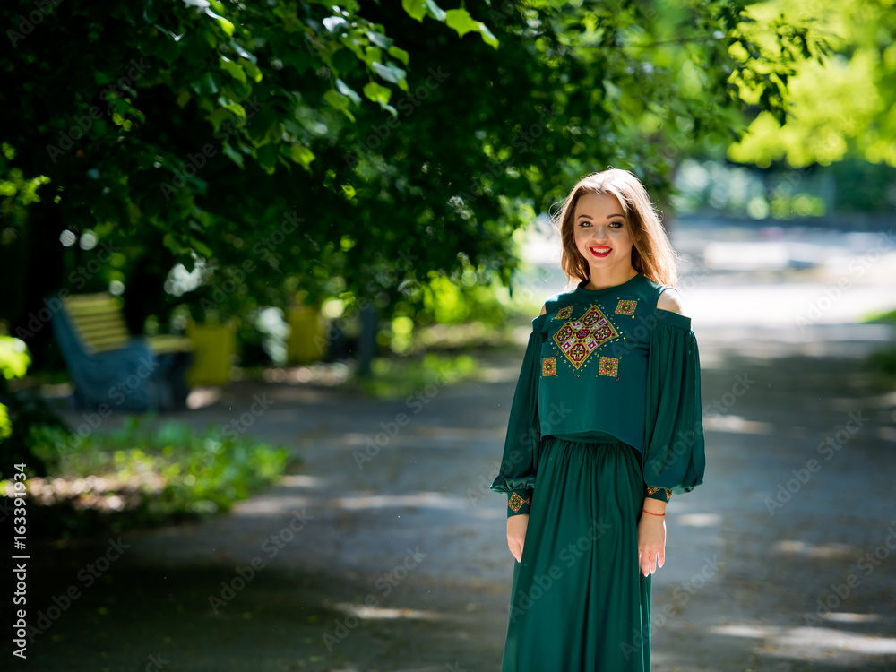 Naklejka premium Young, attractive girl in a green dress in a city park.