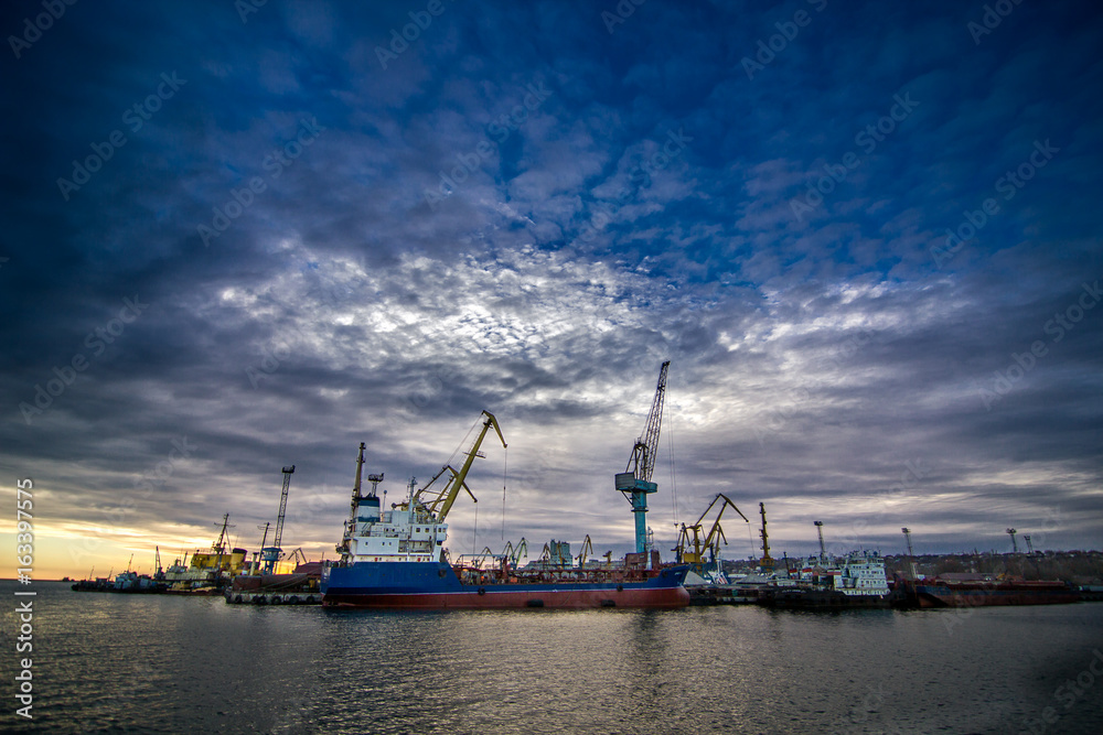 Cargo cranes transship bulk in the dock of Industrial Port on sunset with epic skyline