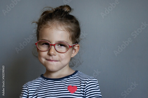 A cunning little girl with red glasses. A child with a smirk