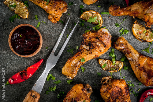 Summer food. Ideas for barbecue, grill party. Chicken legs, wings grilled, fried on fire. With hot chili pepper, lemon and bbq sauce. Dark stone table. Copy space top view