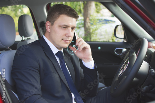 Businessman sitting in his car in a parking lot. Making a phone call with open car doors. Suit and tie businessman sitting in his automobile. © Addoro