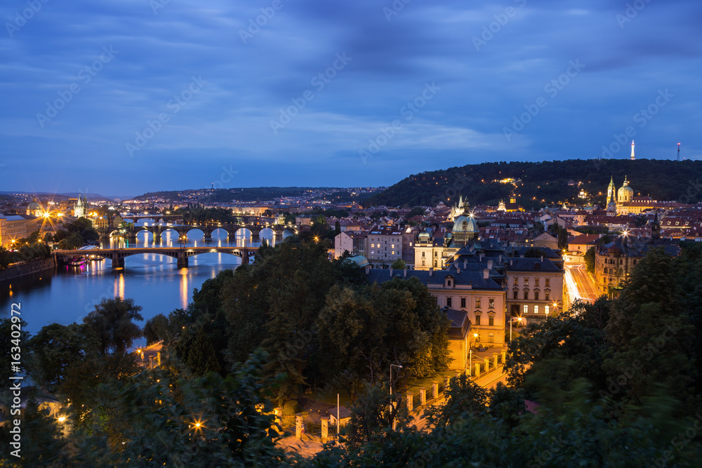 Lit bridges over Vltava River and buildings at the Mala Strana District (Lesser Town) in Prague, Czech Republic, viewed slightly from above at dusk.