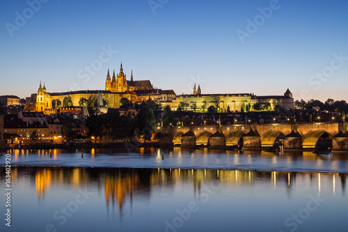 View of the lit Prague (Hradcany) Castle, Charles Bridge (Karluv most) and their reflections on the Vltava River in Prague, Czech Republic, at night.