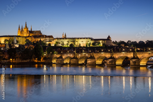 View of the lit Prague (Hradcany) Castle, Charles Bridge (Karluv most) and their reflections on the Vltava River in Prague, Czech Republic, at night.