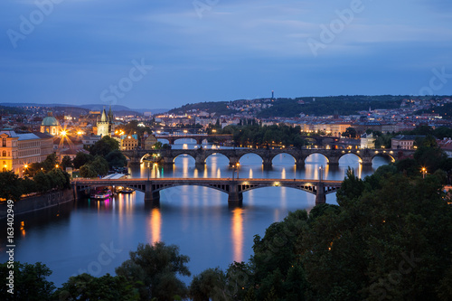 Lit buildings and bridges over Vltava River in Prague, Czech Republic, viewed slightly from above at dusk.