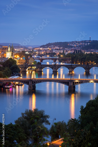 Lit buildings and bridges over Vltava River in Prague, Czech Republic, viewed slightly from above at dusk.