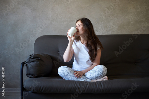 Woman sits on couch and drinking tea