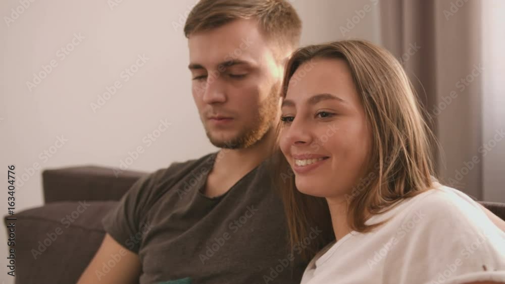 Close up view of attractive young couple sitting on a sofa, covering by coverlet and watching TV in the living room and having fun. Close up view of attractive young couple sitting on a sofa, covering by coverlet and watching TV in the living room and having fun.