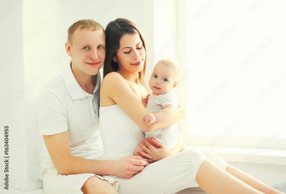 Happy family together, mother and father with baby home in white room near window Happy family together, mother and father with baby home in white room near window