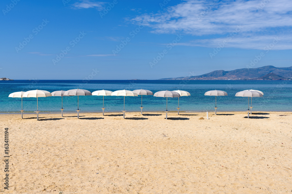 White parasols on Idyllic tropical beach with sand, turquoise sea water and blue sky. Naxos island. Cyclades, Greece. White parasols on Idyllic tropical beach with sand, turquoise sea water and blue sky. Naxos island. Cyclades, Greece.