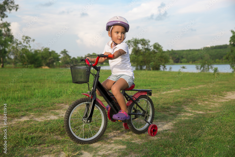 The child riding a bicycle. The kid in a helmet riding a bike in the park. Beautiful baby. The child riding a bicycle. The kid in a helmet riding a bike in the park. Beautiful baby.