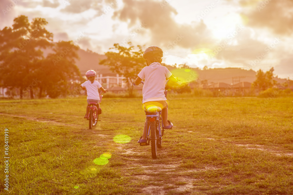 Two child riding a bicycle. The kids in a helmet riding a bike in the park. Beautiful kids. Two child riding a bicycle. The kids in a helmet riding a bike in the park. Beautiful kids.