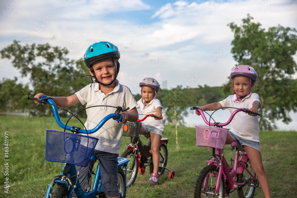 Three child riding a bicycle. The kids in a helmet riding a bike in the park. Beautiful kids. Close up