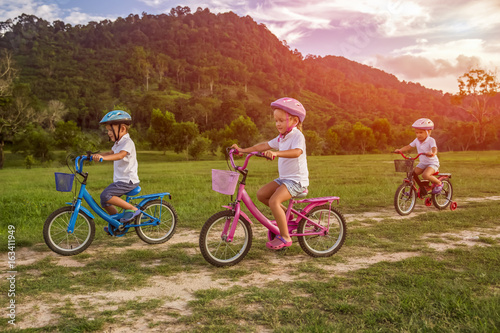 Three child riding a bicycle. The kids in a helmet riding a bike in the park. Beautiful kids.