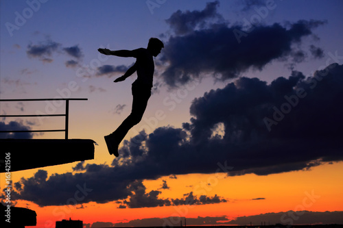 Man is jumping from edge of roof. Clouds and sunset