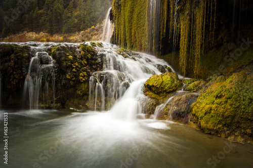 A waterfall runs down saturated, green moss on a stormy afternoon.