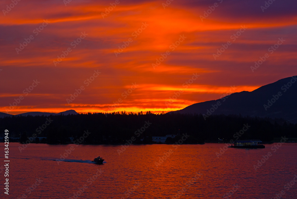 Scarlet sunset over the city of Vancouver, BC, Canada. Mountains landscape during sunset with water and high pine trees on horizon.
